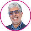 Smiling man with gray hair and beard wearing blue glasses and a blazer, pictured in front of a white background with a pink circular border, representing a collaborative approach essential in the digital era.